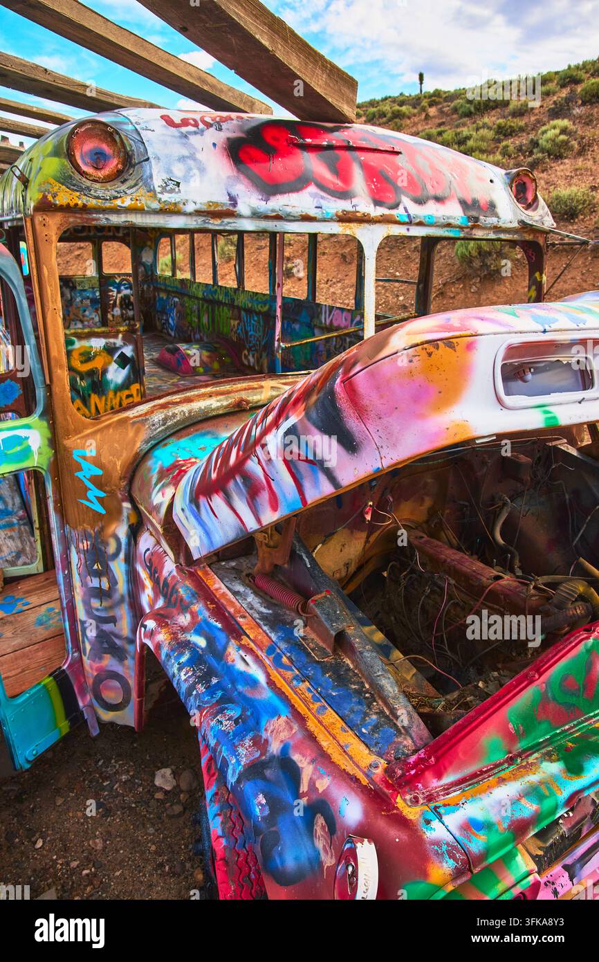 Graffiti vividi coprono un veicolo abbandonato nella Foresta Internazionale delle Auto a Goldfield, Nevada. Il cofano aperto e l'interno vuoto evocano creatori di arte urbana Foto Stock