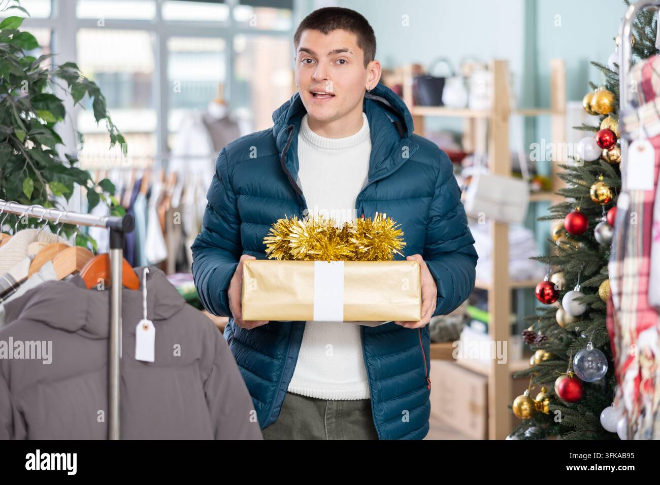 Cliente uomo con una scatola regalo elegante tra le mani. Preparativi per la vigilia di Capodanno, ampia selezione di regali piacevoli e pratici in un negozio di abbigliamento Foto Stock