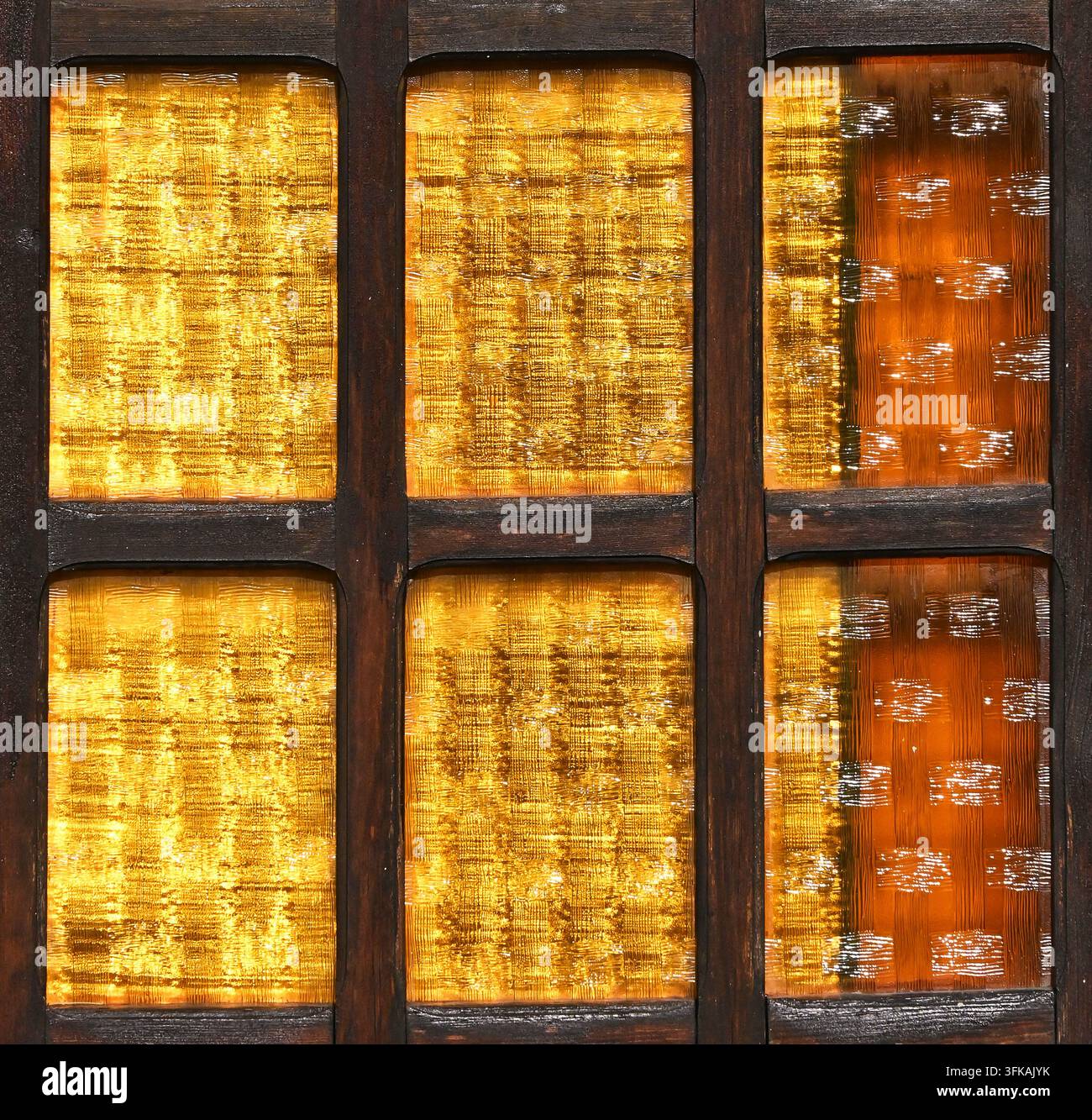 Fotografia macro di una finestra decorativa strutturata con pannelli di vetro a motivi dorati e ambrati incorniciati da listelli di legno scuro. Foto Stock