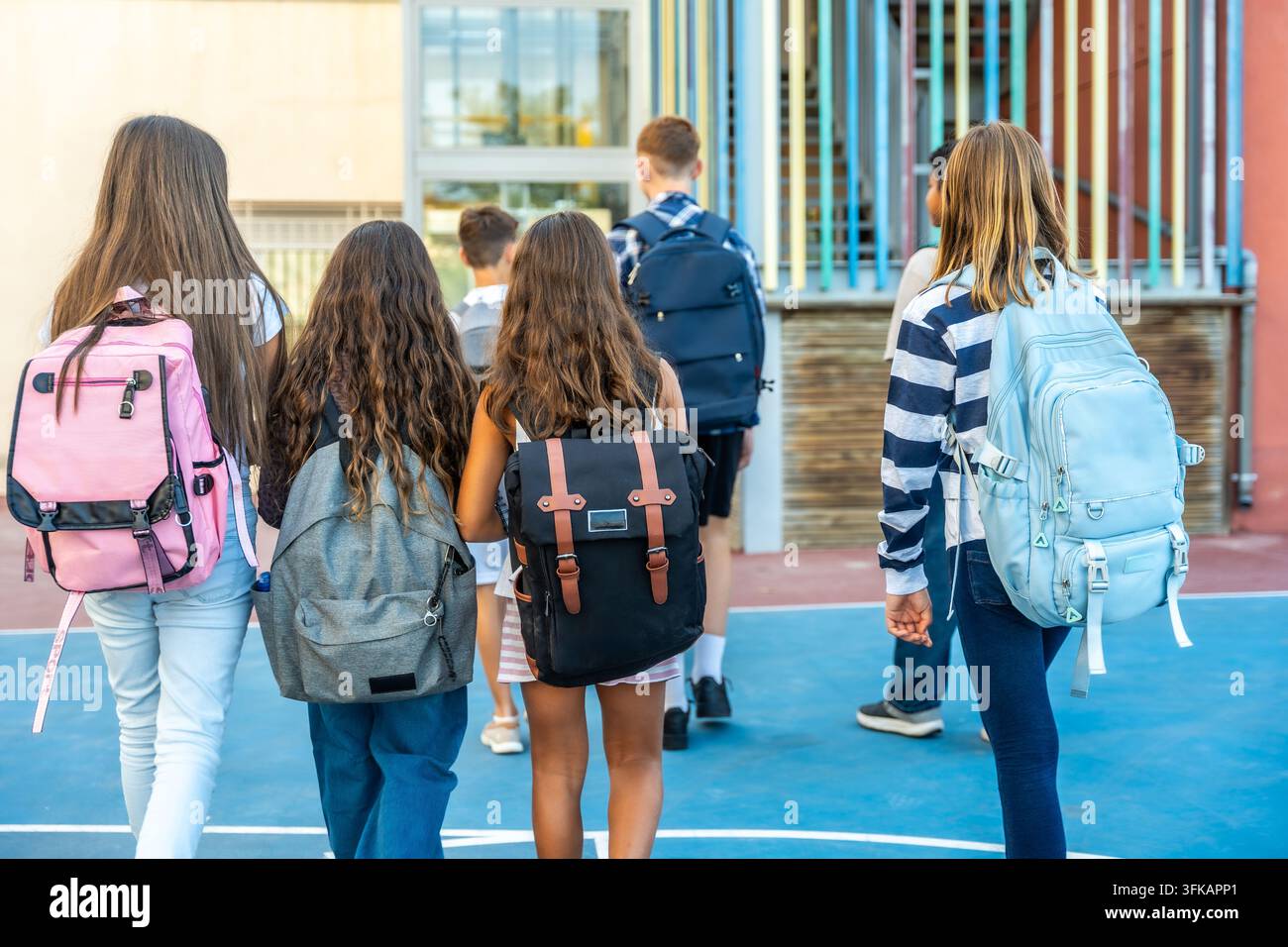 Studenti con zaini che camminano verso l'ingresso dell'edificio scolastico Foto Stock
