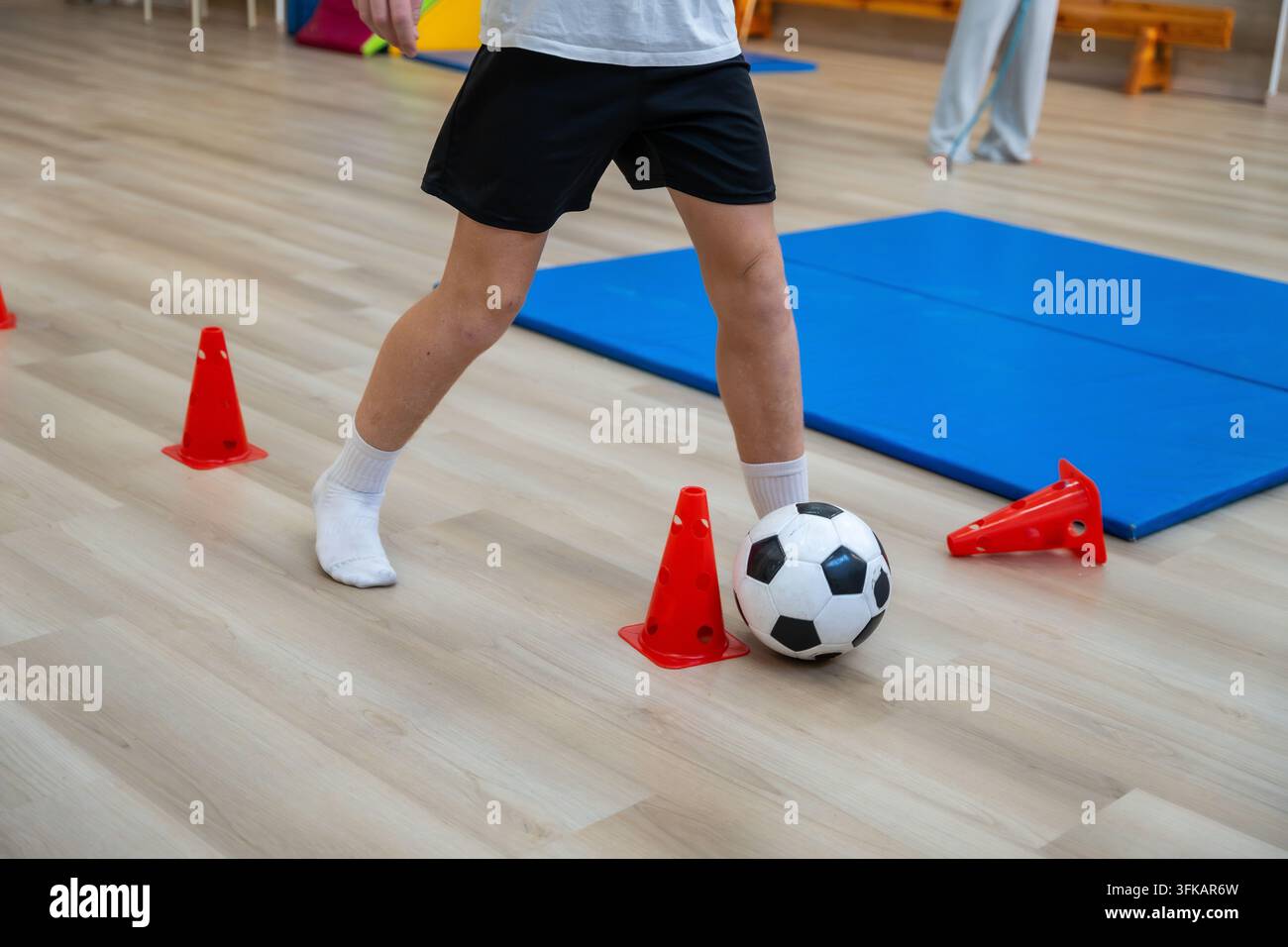 Bambino che allena le abilità di calcio dribblando la palla tra i coni Foto Stock