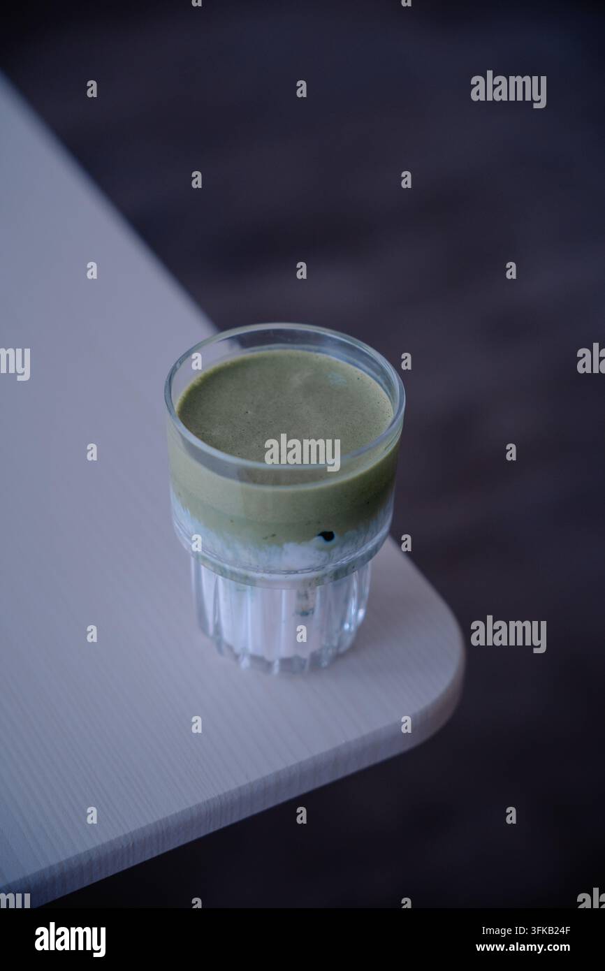 Latte freddo al tè verde matcha servito in un bicchiere a nervature trasparenti sul tavolo del caffè. Foto Stock