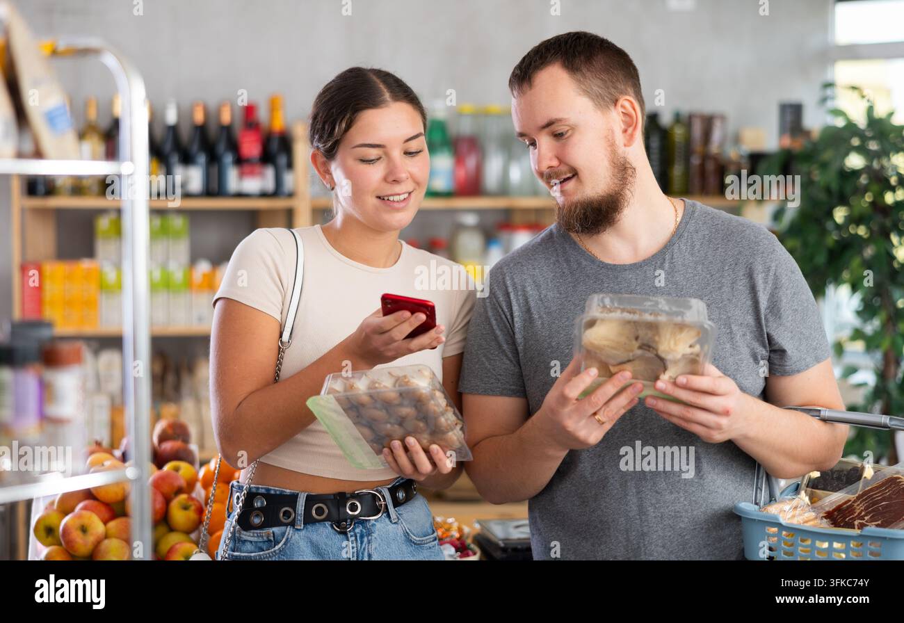Coppia acquirente che esegue la scansione del codice QR o del codice a barre dei funghi nel supermercato Foto Stock