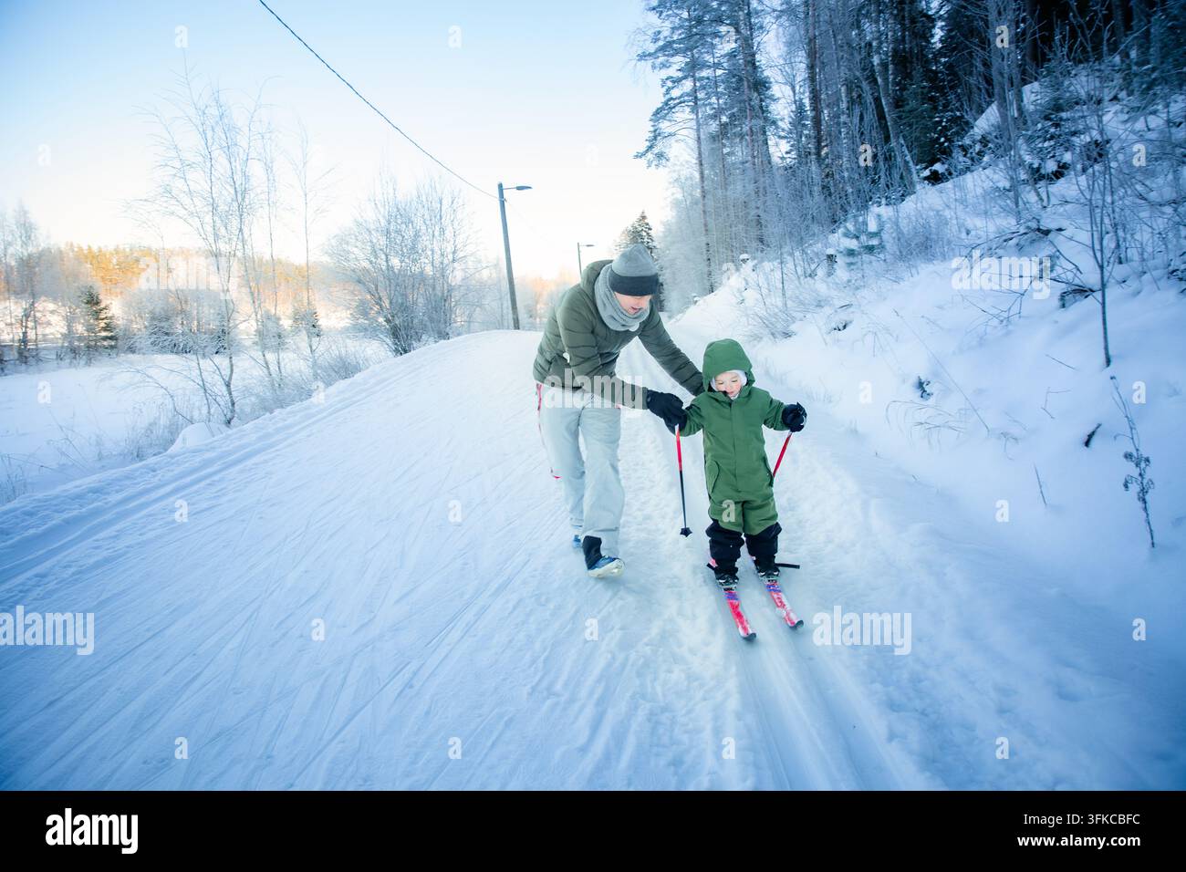 Un padre aiuta il suo bambino a imparare a fare sci di fondo su un sentiero innevato nella regione di Helsinki, in Finlandia, durante un'uscita familiare attiva in inverno. Foto Stock