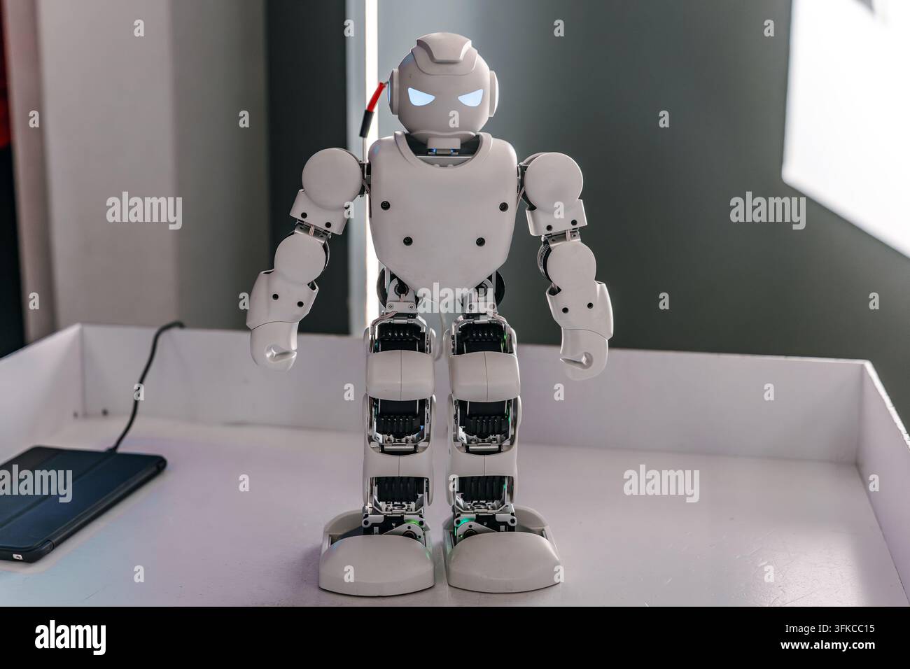 Robotto umanoide bianco con occhi blu luminosi in piedi su un tavolo Foto Stock