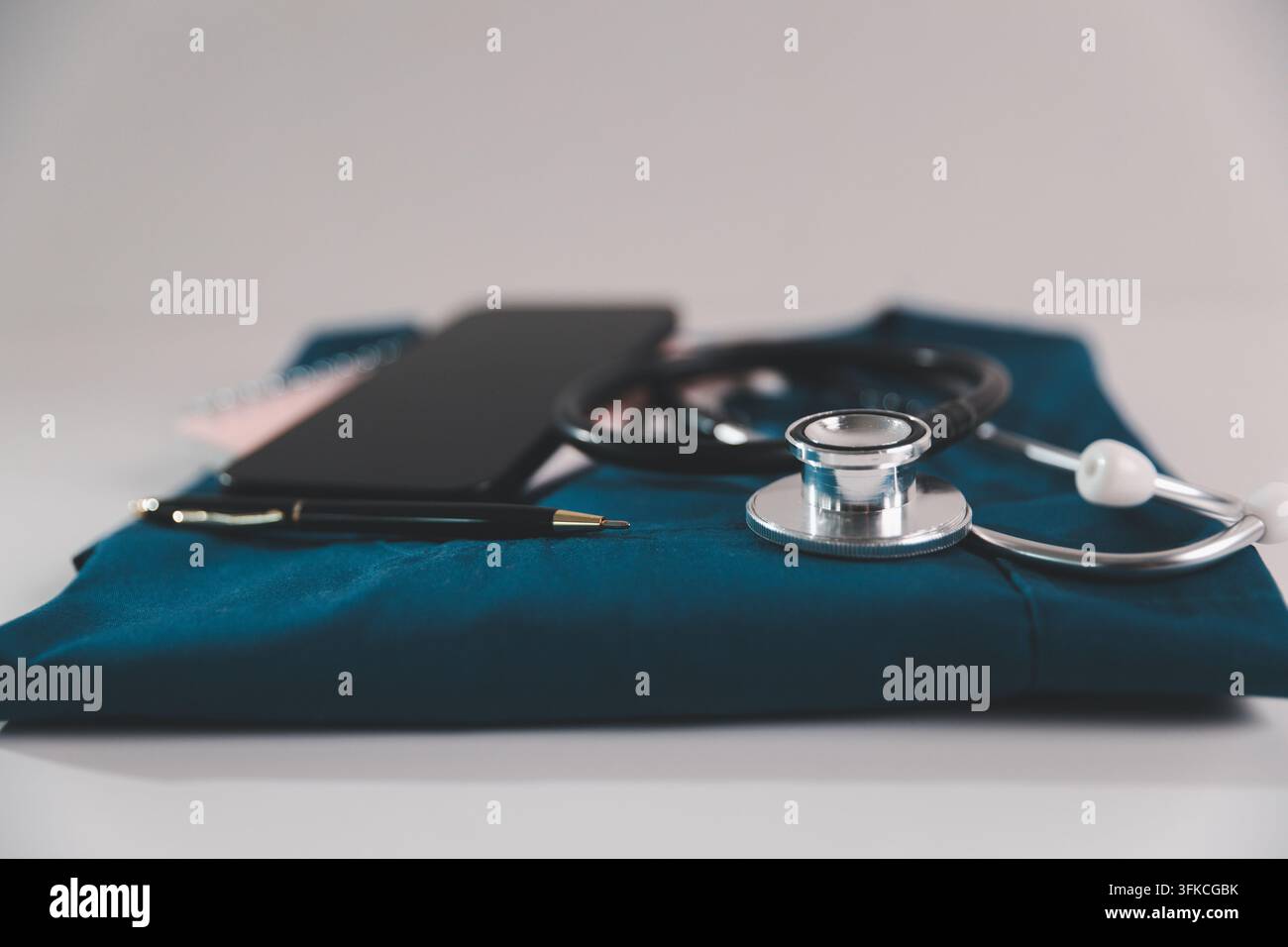 Stetoscopio, smartphone e penna su camici medici piegati, rappresentanti l'assistenza sanitaria mobile, la telemedicina, la tecnologia sanitaria digitale e la clinica moderna Foto Stock