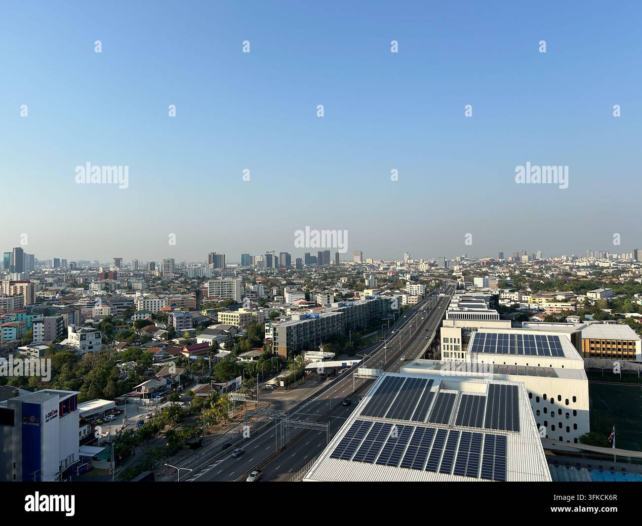 Vista elevata del paesaggio urbano di Bangkok con edifici residenziali e commerciali, una grande autostrada e pannelli solari sui tetti sotto un cielo azzurro limpido. - Immagine stock catturata con smartphone