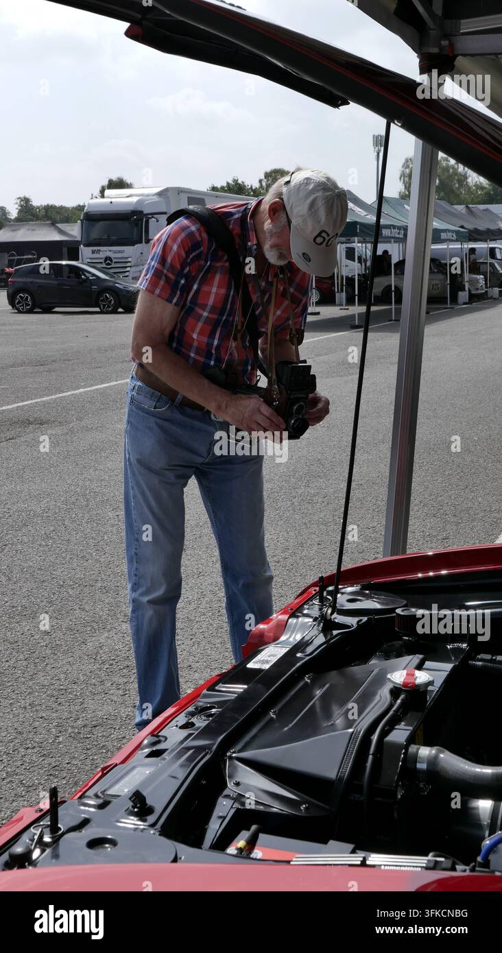 Un anziano che fotografa un'auto utilizzando una fotocamera medio formato a livello della vita Foto Stock