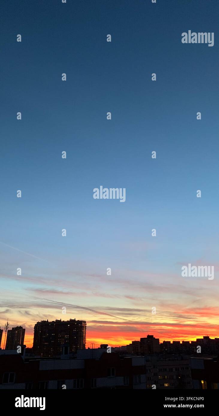 Scatto verticale all'aperto di un drammatico cielo al tramonto colorato che passa dal blu profondo all'arancione brillante sopra le silouette scure di edifici residenziali urbani Foto Stock