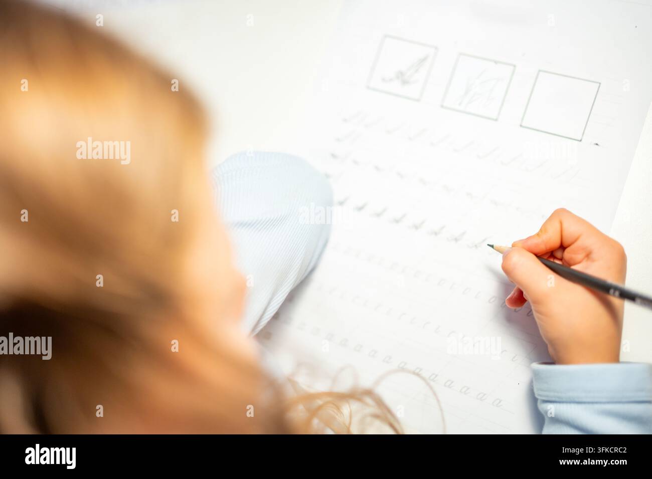 Una bambina di prima elementare pratica la calligrafia con una matita in un quaderno scolastico. Il bambino impara a scrivere lettere durante l'educazione precoce con una concentrazione selettiva e Foto Stock