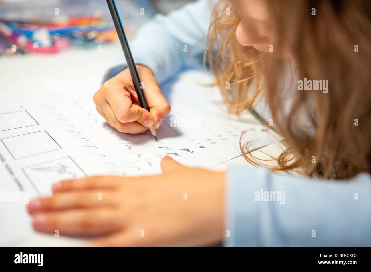 Una bambina di prima elementare pratica la calligrafia con una matita in un quaderno scolastico. Il bambino impara a scrivere lettere durante l'educazione precoce con una concentrazione selettiva e Foto Stock