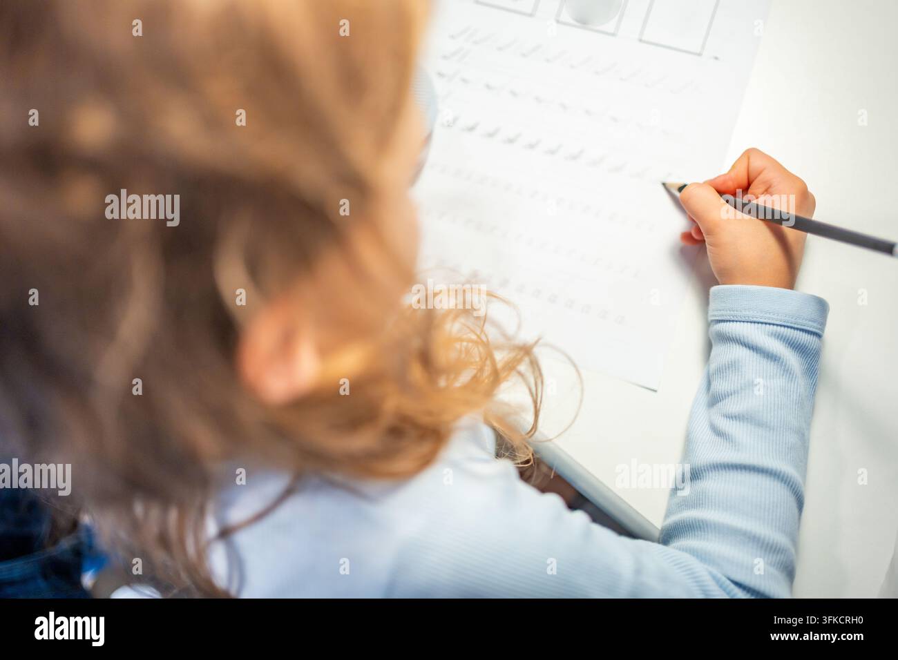 Una bambina di prima elementare pratica la calligrafia con una matita in un quaderno scolastico. Il bambino impara a scrivere lettere durante l'educazione precoce con una concentrazione selettiva e Foto Stock