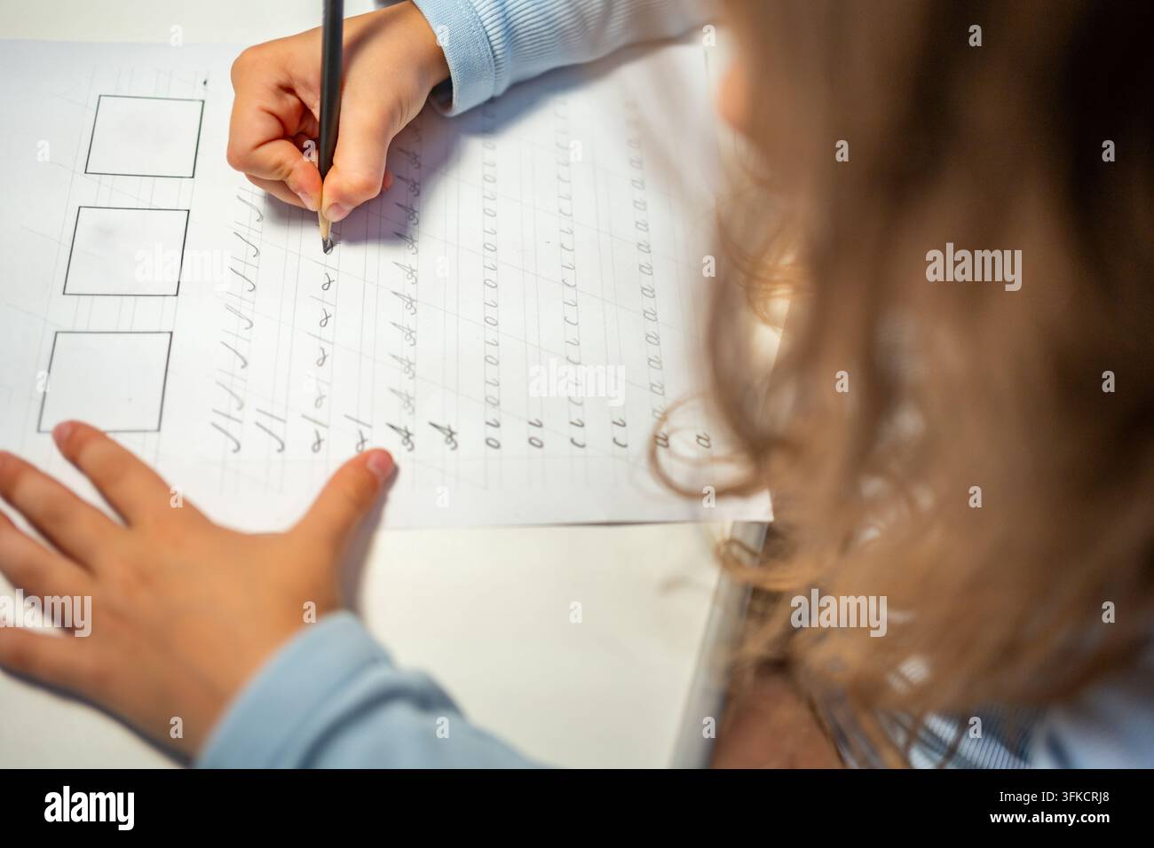 Una bambina di prima elementare pratica la calligrafia con una matita in un quaderno scolastico. Il bambino impara a scrivere lettere durante l'educazione precoce con una concentrazione selettiva e Foto Stock