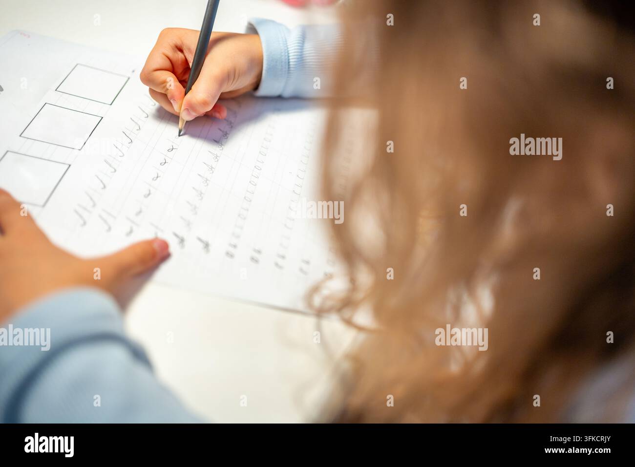 Una bambina di prima elementare pratica la calligrafia con una matita in un quaderno scolastico. Il bambino impara a scrivere lettere durante l'educazione precoce con una concentrazione selettiva e Foto Stock