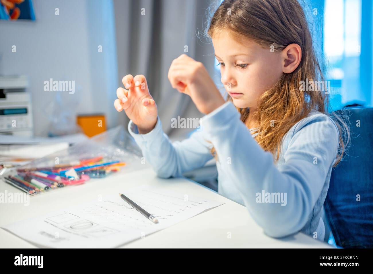 Bambina di prima elementare allunga le dita stanche durante la pratica della calligrafia a casa. La bambina si prende una pausa dallo scrivere per alleviare l'affaticamento della mano con selettivo Foto Stock