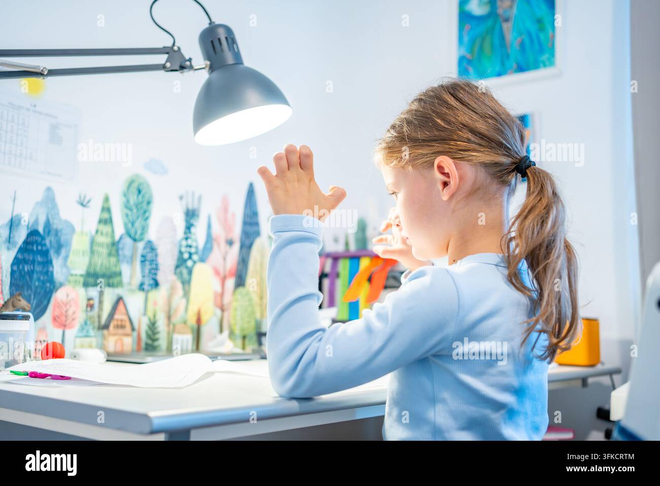 Bambina di prima elementare allunga le dita stanche durante la pratica della calligrafia a casa. La bambina si prende una pausa dallo scrivere per alleviare l'affaticamento della mano con selettivo Foto Stock