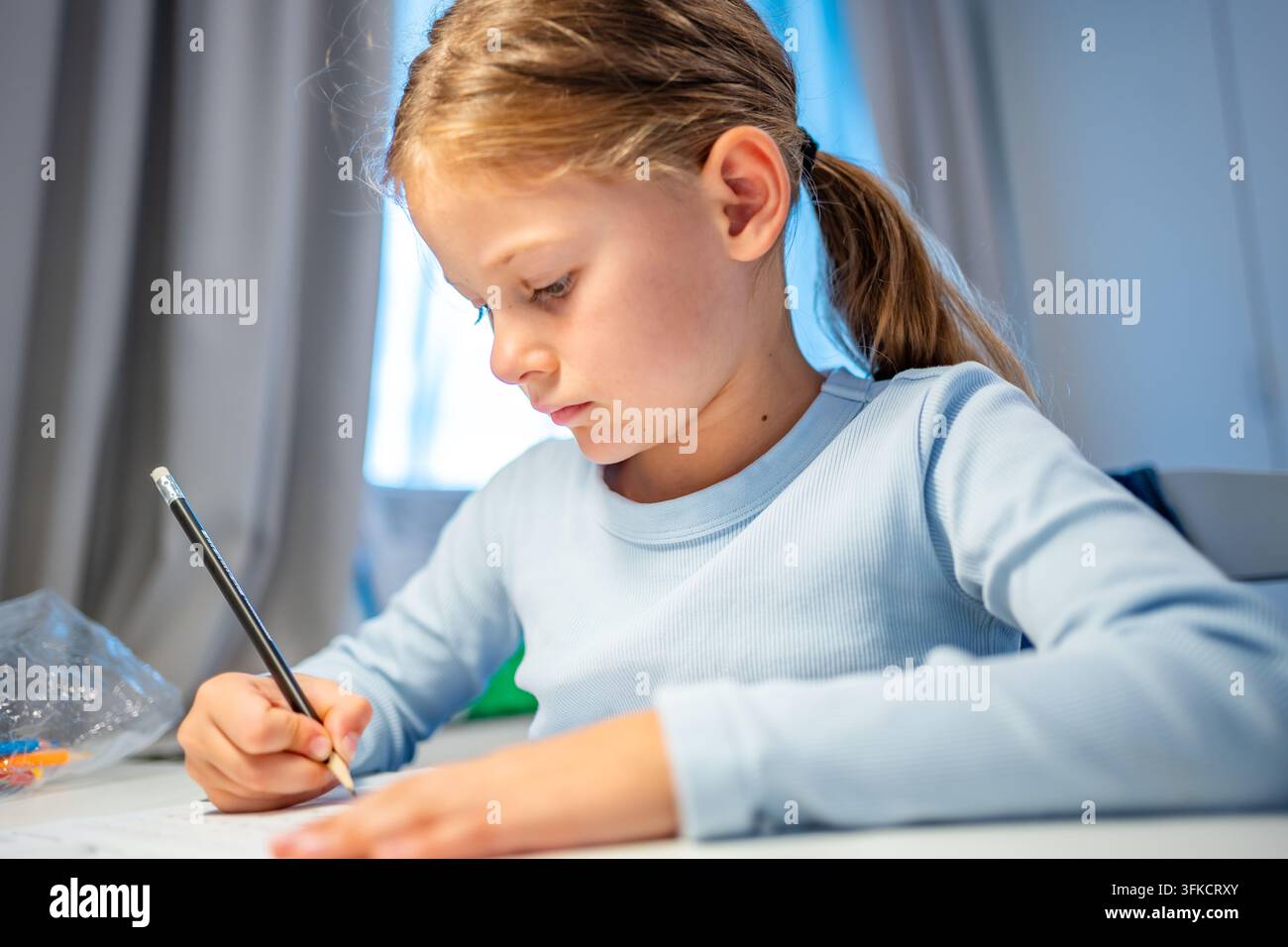 Bambina di prima elementare scrive con una matita mentre studia a casa. Un bambino concentrato sviluppa capacità di scrittura e apprendimento con attenzione selettiva e profondità ridotta Foto Stock