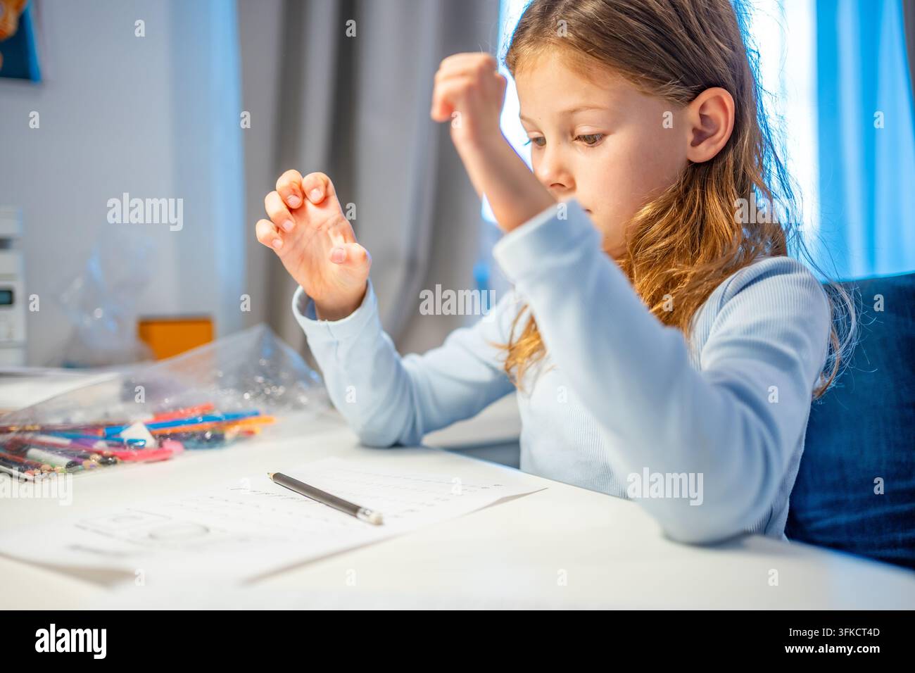 Bambina di prima elementare allunga le dita stanche durante la pratica della calligrafia a casa. La bambina si prende una pausa dallo scrivere per alleviare l'affaticamento della mano con selettivo Foto Stock