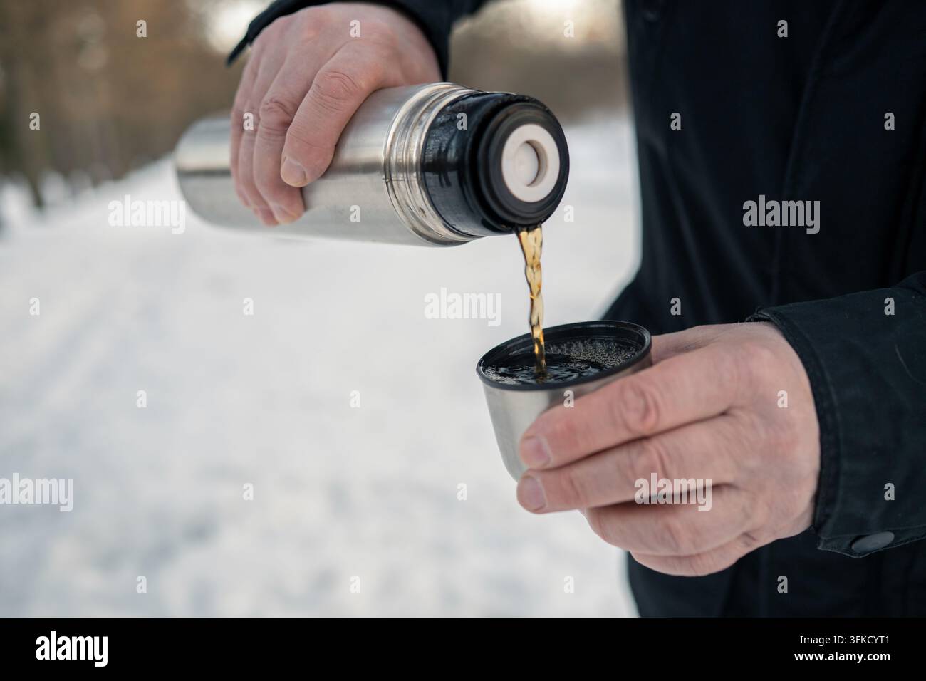 Bevanda calda versata da una thermos in acciaio inossidabile in una tazza di metallo all'aperto nella neve, viaggio invernale, concetto di bevanda riscaldante e rinfresco. Foto Stock
