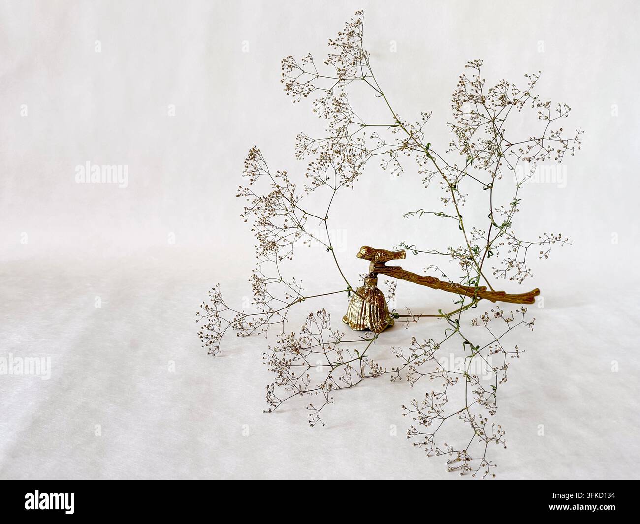 Ornamento vintage a forma di uccello dorato e campana con delicato gipsofila essiccata e sfondo bianco morbido con spazio per il testo Foto Stock