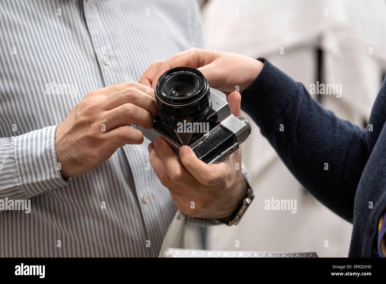 Doha, Qatar - 8 ottobre 2026: Primo piano di mani che esaminano una classica fotocamera reflex Zenit vintage dotata di obiettivo fisso Helios 44M-4. Foto Stock