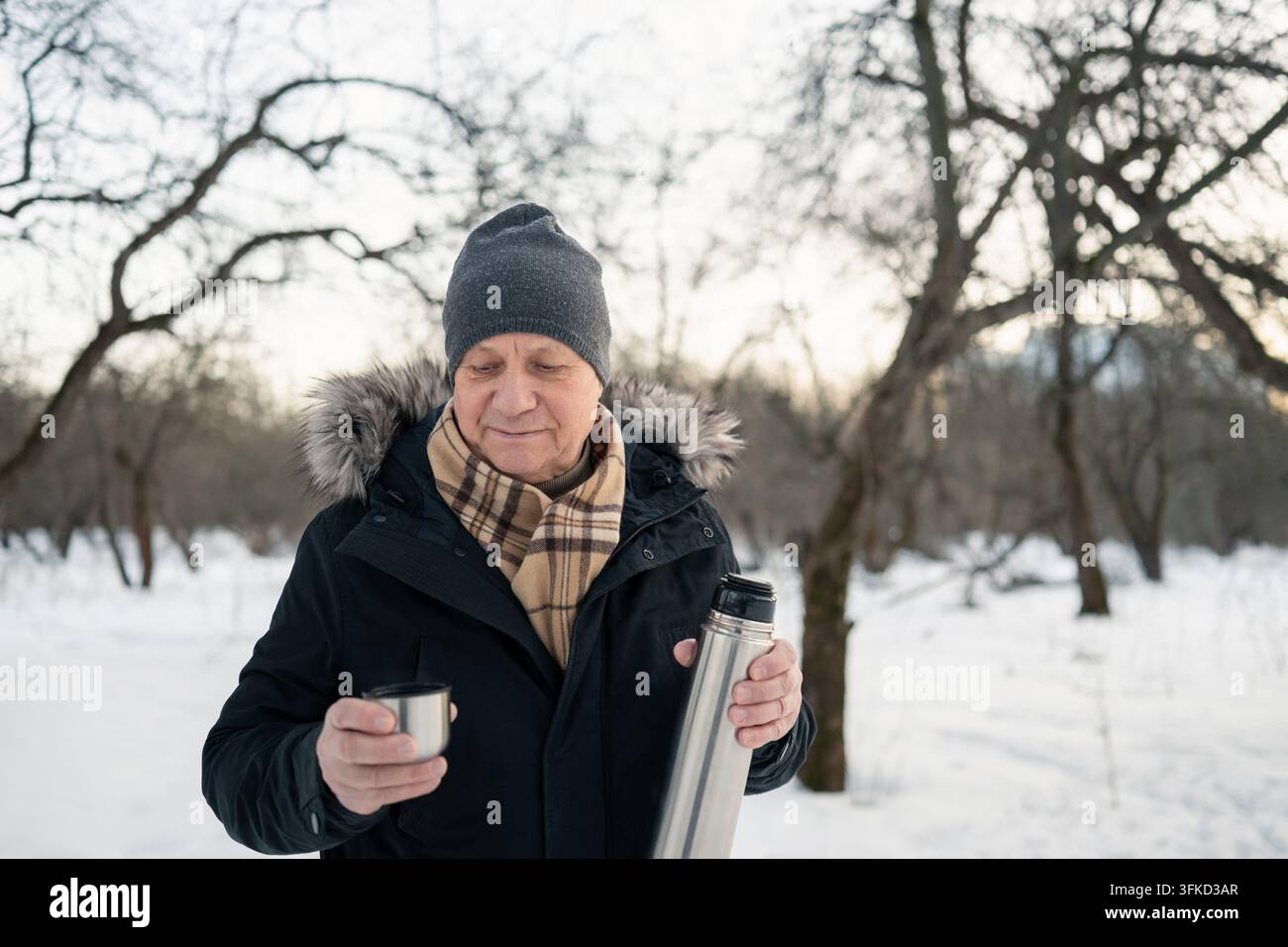 Uomo maturo che beve una bevanda calda da una tazza termica in inverno Foto Stock