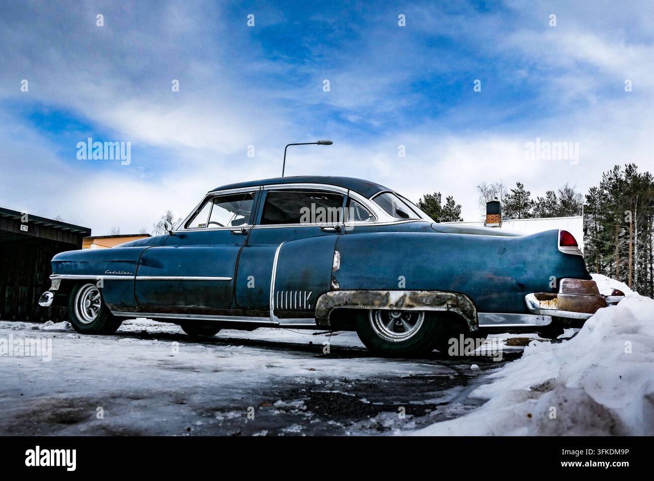 Sedan classico blu patinato parcheggiato accanto a una strada innevata in inverno Foto Stock