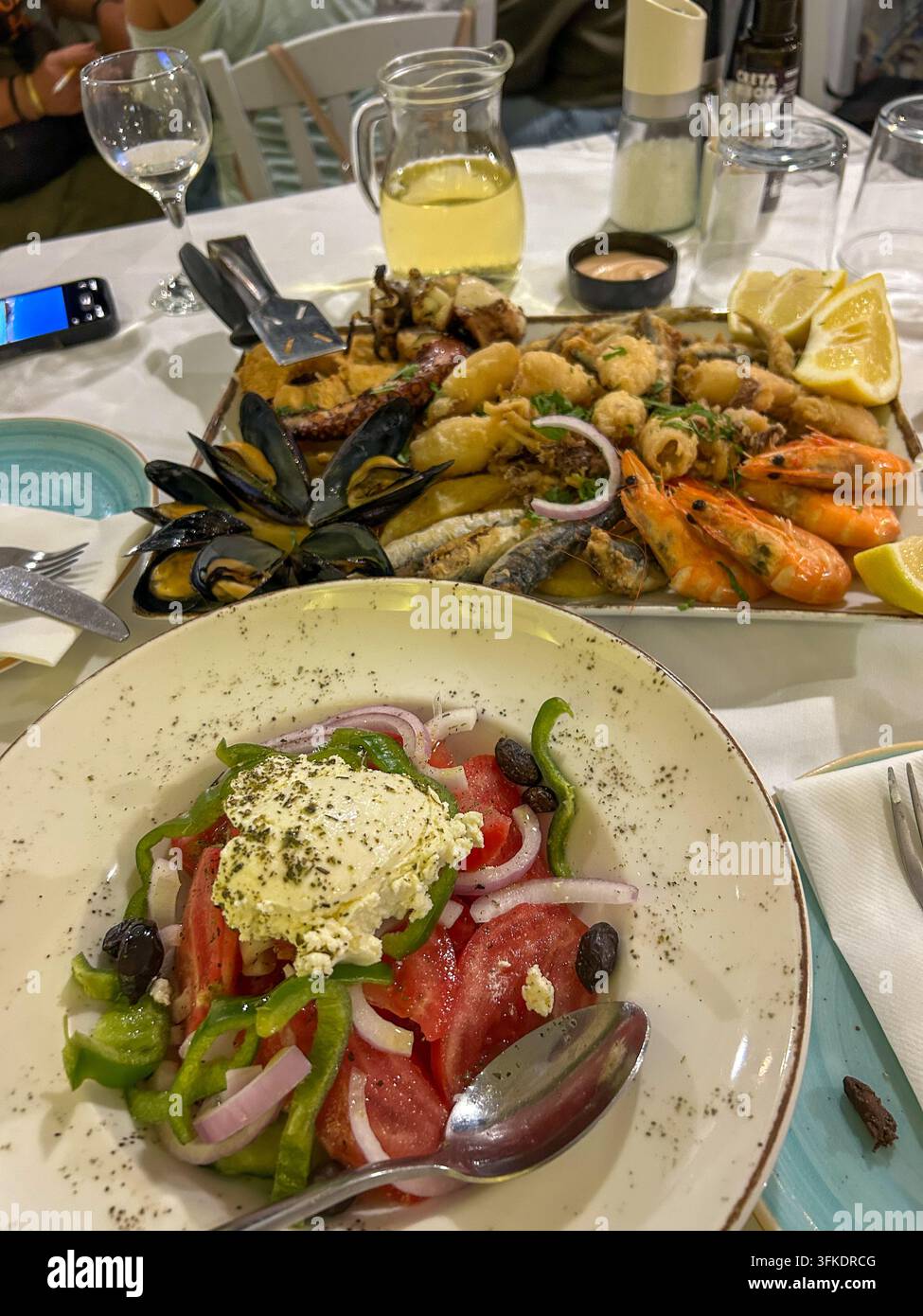 Insalata greca tradizionale con formaggio feta, accompagnata da un vassoio di frutti di mare freschi con gamberetti, cozze, calamari e pesce fritto, Creta. - Immagine stock catturata con smartphone