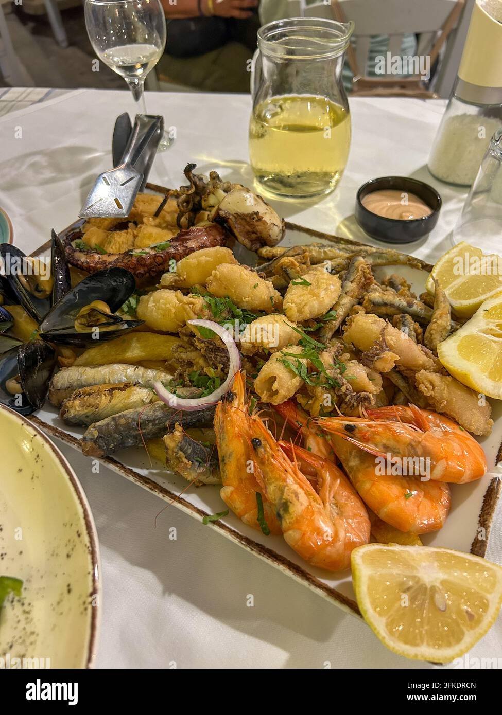 Generoso vassoio di frutti di mare con polpo grigliato, calamari fritti, cozze, gamberi e acciughe, servito con spicchi di limone freschi. - Immagine stock catturata con smartphone