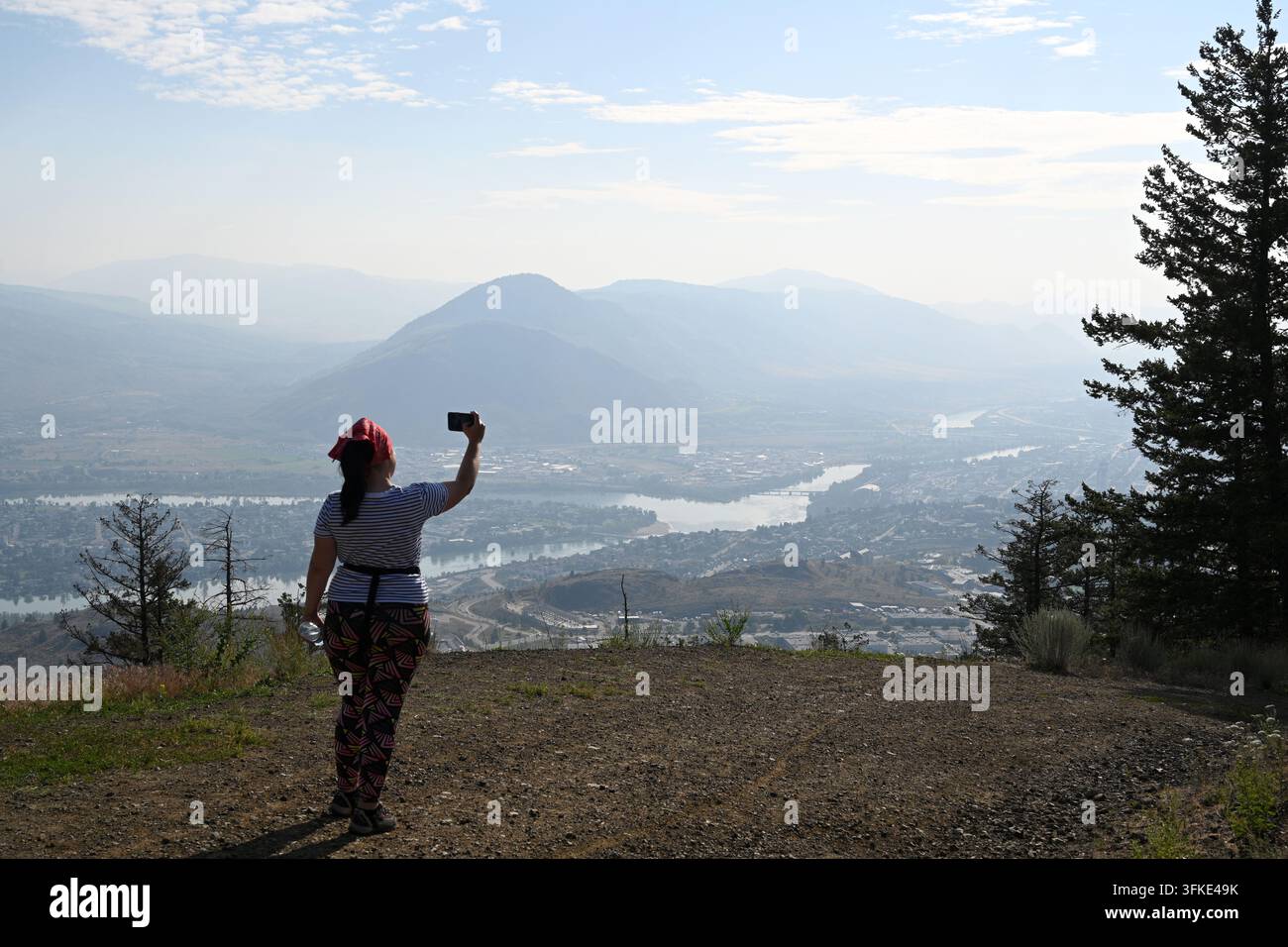 Kamloops, Columbia Britannica, Canada — 9 luglio 2026: Una donna scatta una foto della città di Kamloops, Columbia Britannica, Canada, con il suo smartphone. Foto Stock