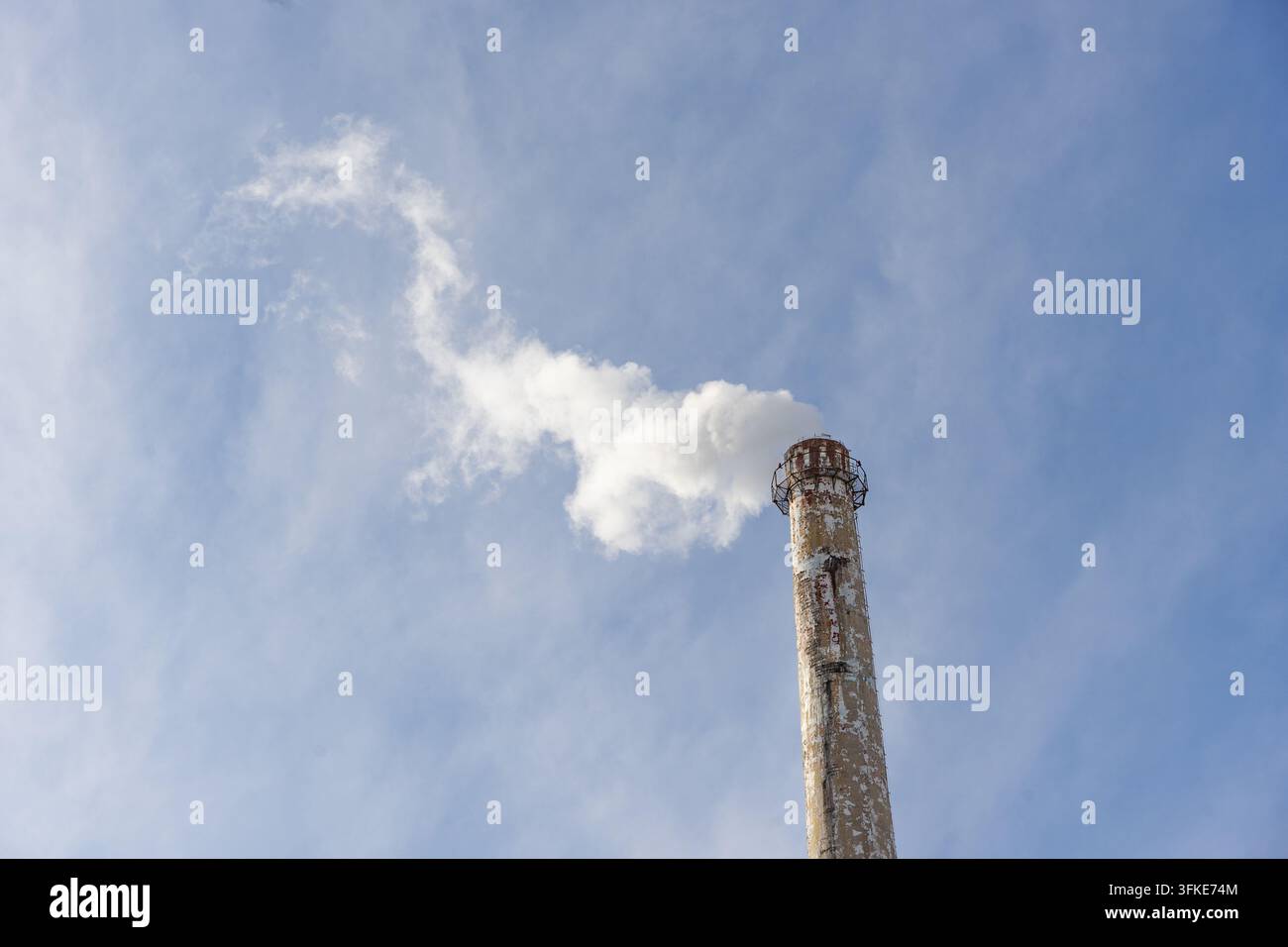 Fumo bianco che si arriccia fuori dalle ciminiere industriali e si disperde nel cielo azzurro Foto Stock