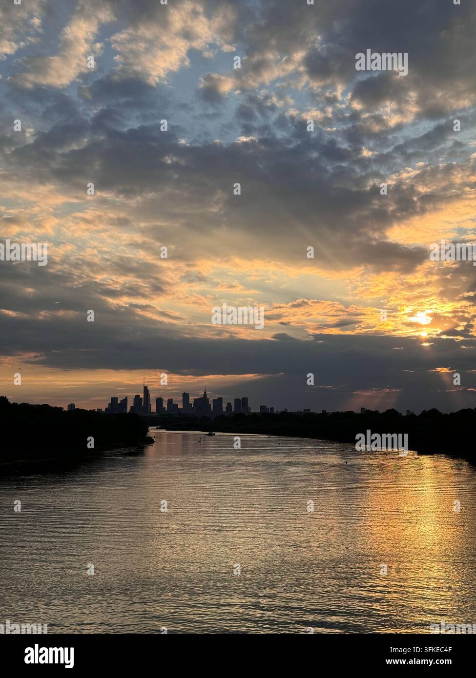 Panorama di Varsavia visto attraverso il fiume Vistola al tramonto, con nuvole drammatiche, riflessi dorati sull'acqua e raggi di sole sulla capitale polacca - Immagine stock catturata con smartphone