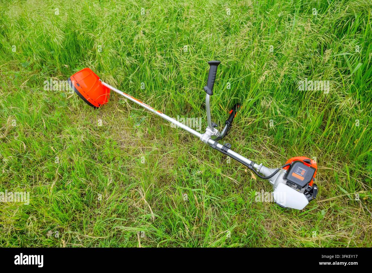 Un tagliaerba arancione giace nell'erba prima che il terreno venga falciato Foto Stock