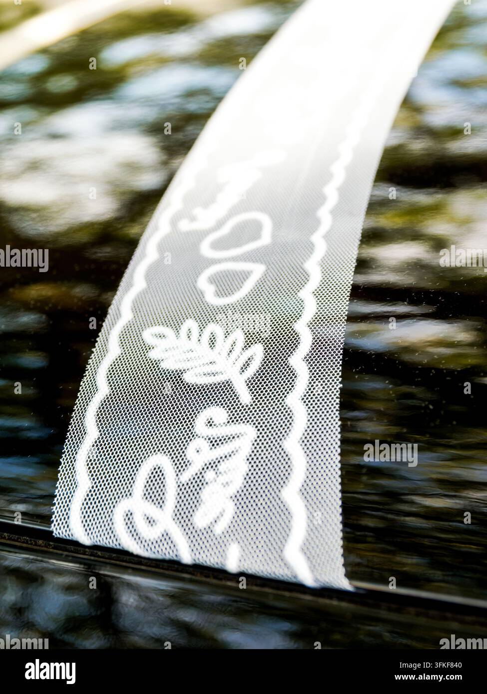 Nastro di pizzo decorativo bianco con motivi a cuore e floreali riflesso su una superficie scura Foto Stock