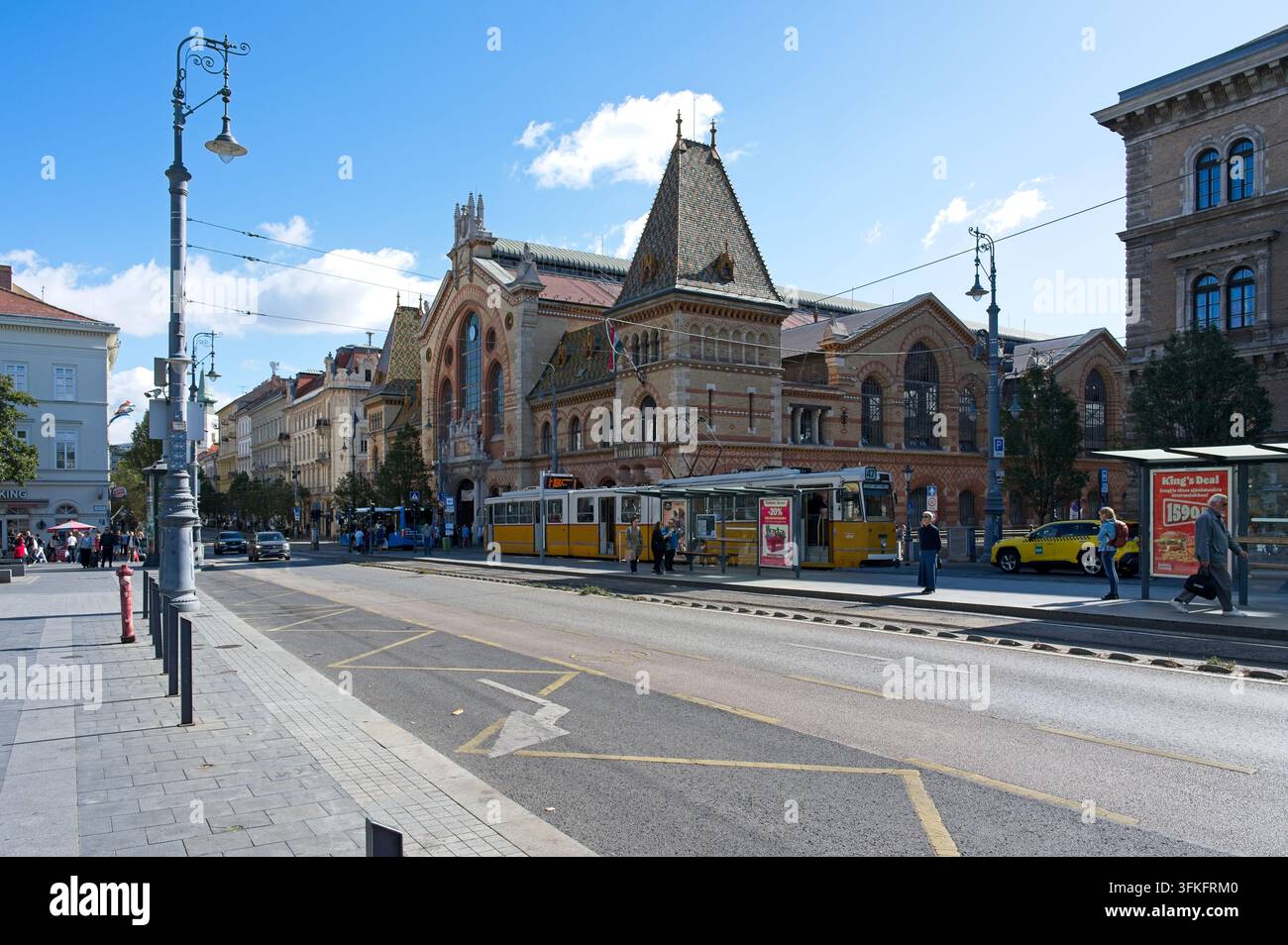 Budapest, Ungheria - 21 settembre 2026: Tram giallo fermato alla stazione di Fovam ter davanti alla storica Grande Hall del Mercato. Foto Stock