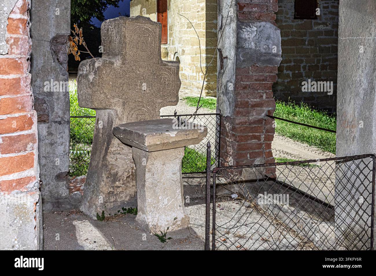 Croce in pietra storica e consumata e piccolo altare all'interno di un'antica struttura in mattoni recintata in un sito religioso di notte, cantina, villaggio di Rojljevac, Serbia Foto Stock