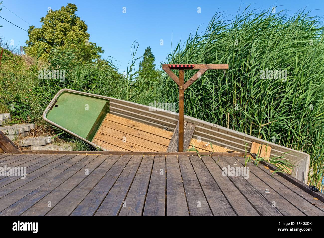 Molo di legno e vecchia barca sulla riva ricoperta di canne verdi sull'acqua, paesaggio naturale tranquillo, campagna. Foto Stock