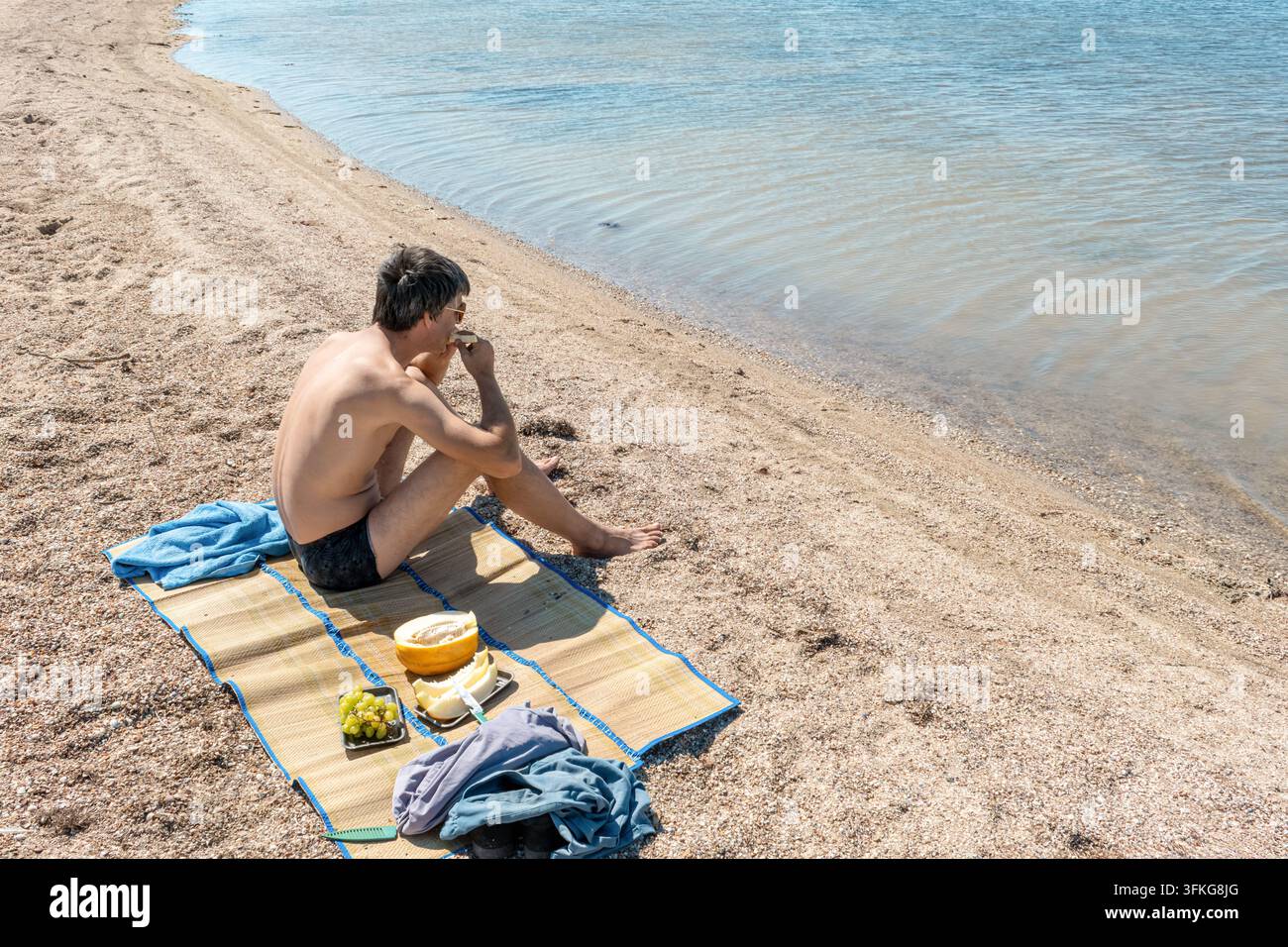 Uomo che mangia melone fresco durante un picnic sulla spiaggia sulla riva del lago Burnas a Lebedivka, regione di Odessa. Sfondo di vacanza estiva rilassata e viaggio Foto Stock