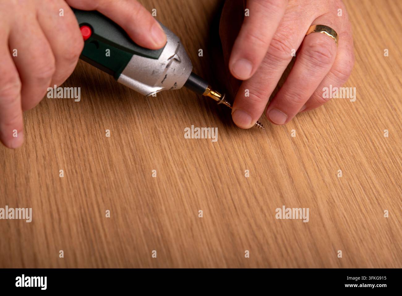 Dita che tengono una vite su un avvitatore senza filo su un tavolo di legno. Foto Stock