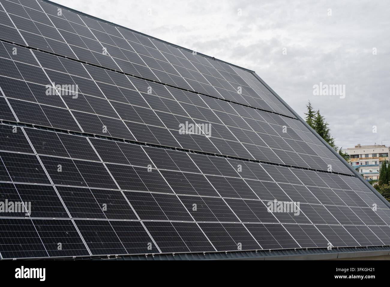 Uno scatto in bianco e nero, con prospettiva a bassa angolazione, di una grande disposizione inclinata di pannelli solari fotovoltaici su un tetto con un condominio a più piani sullo sfondo Foto Stock