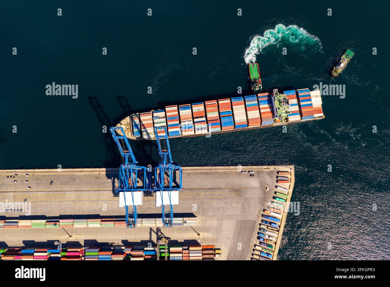 Grande nave portacontainer carica di casse colorate in arrivo al porto di Perama, Attiki, Grecia, guidata da rimorchiatori in un affollato porto commerciale — vista aerea o Foto Stock