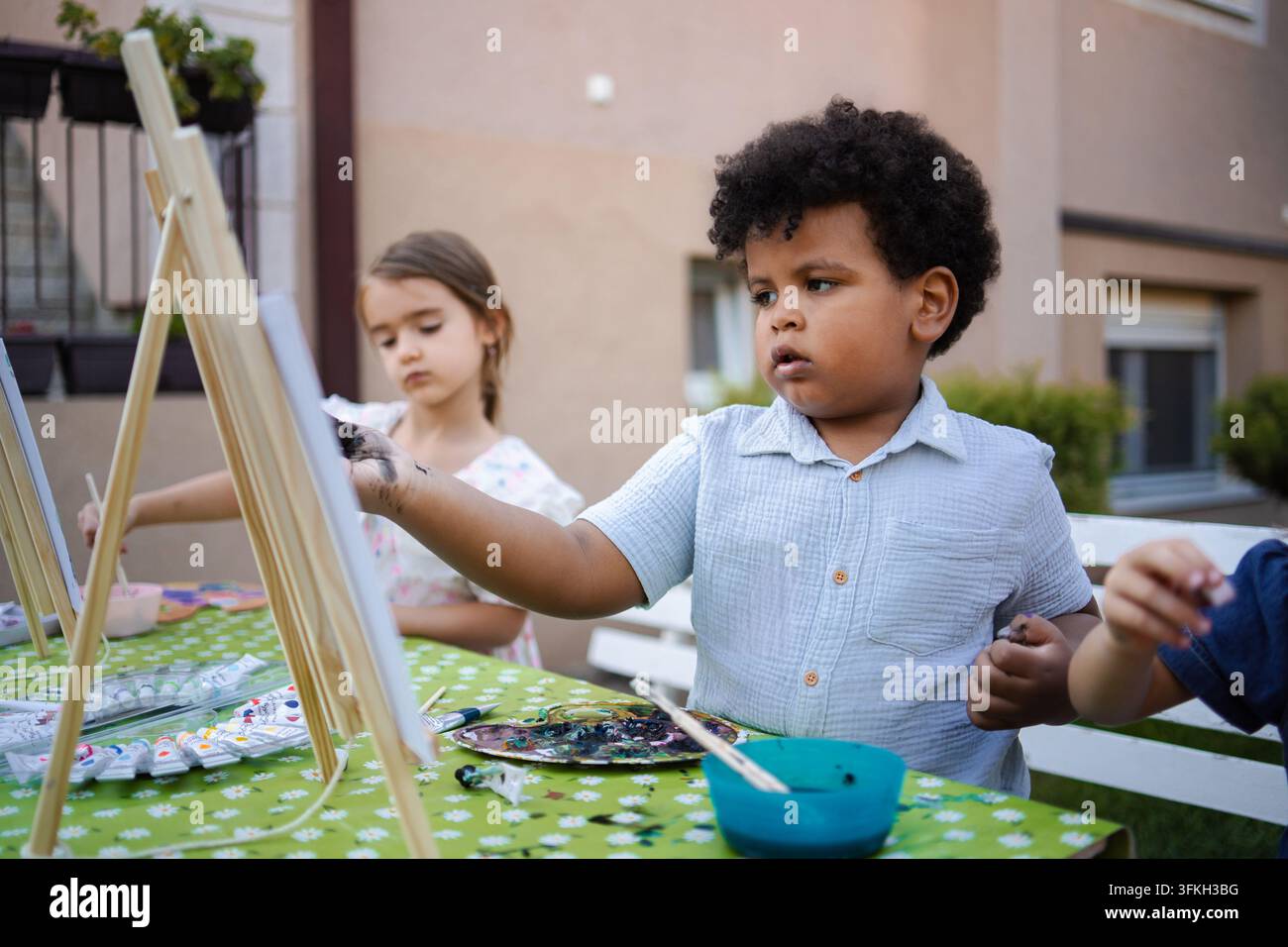 Bambini che dipingono su cavalletti all'aperto e si divertono con un'attività artistica Foto Stock