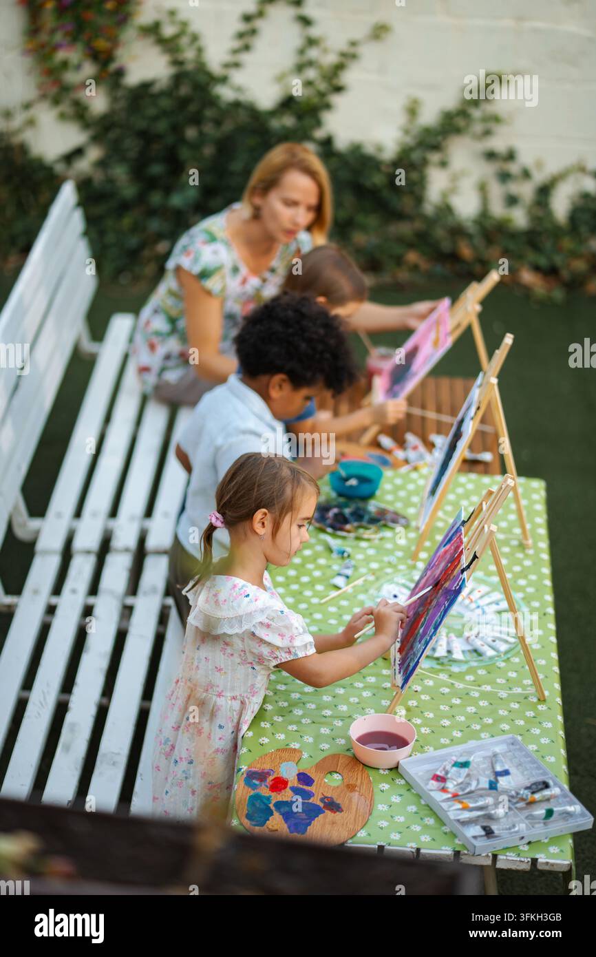 Bambini diversi che imparano a dipingere con l'insegnante all'aperto Foto Stock