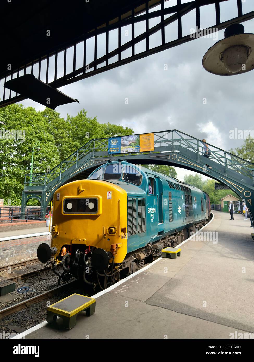 Una locomotiva diesel-elettrica britannica di classe 37 con il numero 37264 in livrea blu British Rail, che passa un ponte pedonale ed entra a Pickering - Immagine stock catturata con smartphone