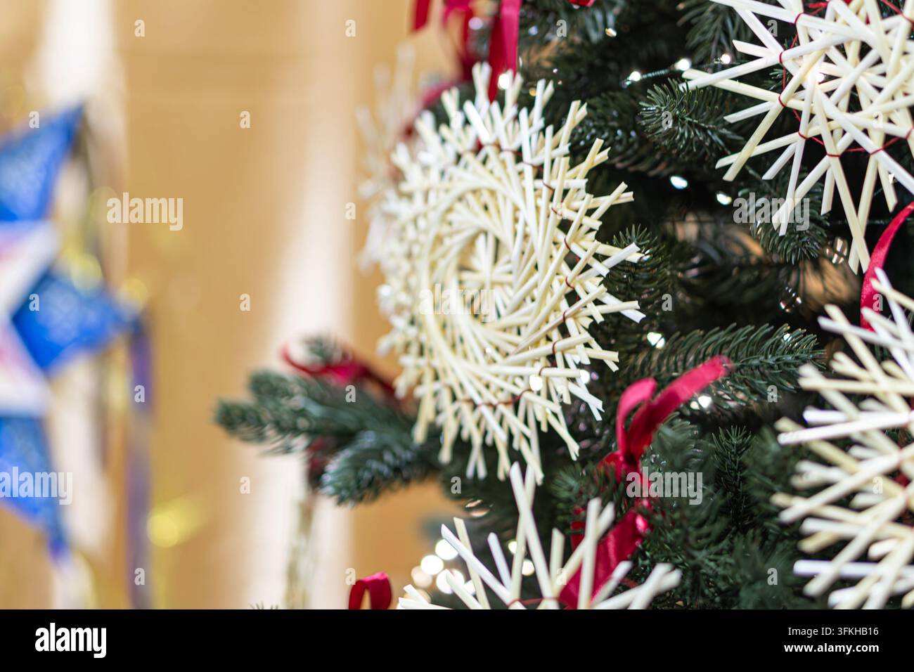 Albero di Natale in primo piano, fogliame verde denso, ornamenti di paglia bianchi a forma di stella, illuminazione ambientale calda, ambientazione interna festosa, stile rustico fatto a mano, Foto Stock