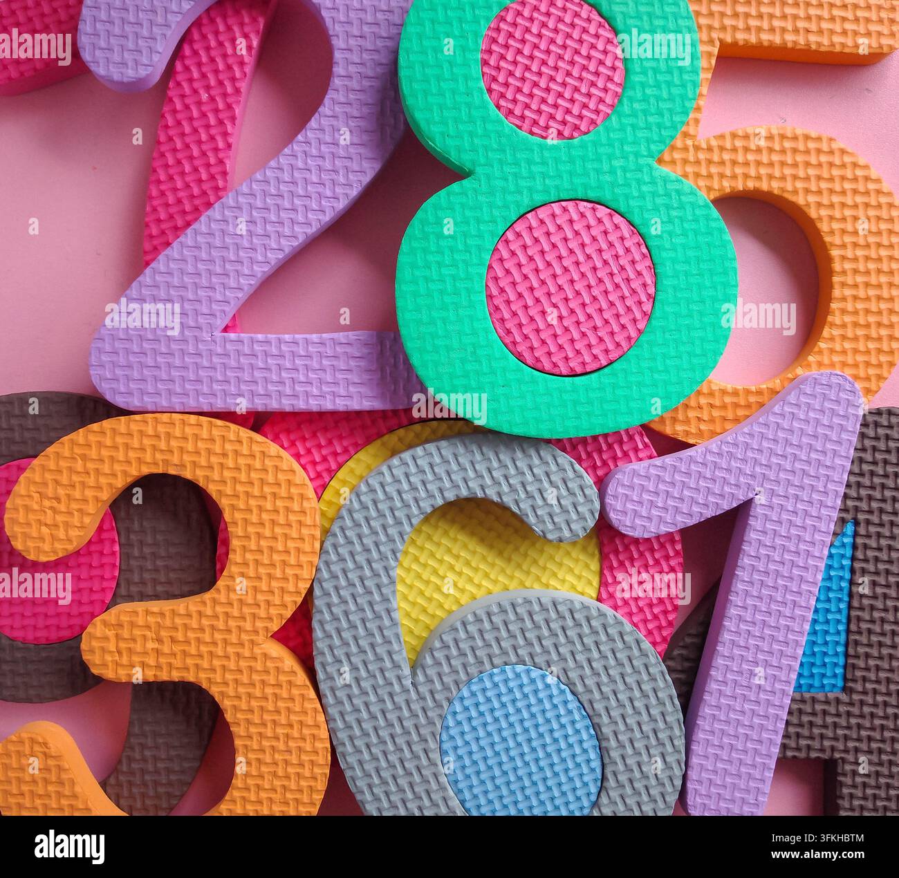 Sfondo di numeri colorati. Numeri di puzzle in schiuma colorati ammucchiati su uno sfondo rosa. Sfondo a mosaico di numeri di puzzle in schiuma colorati. Foto Stock