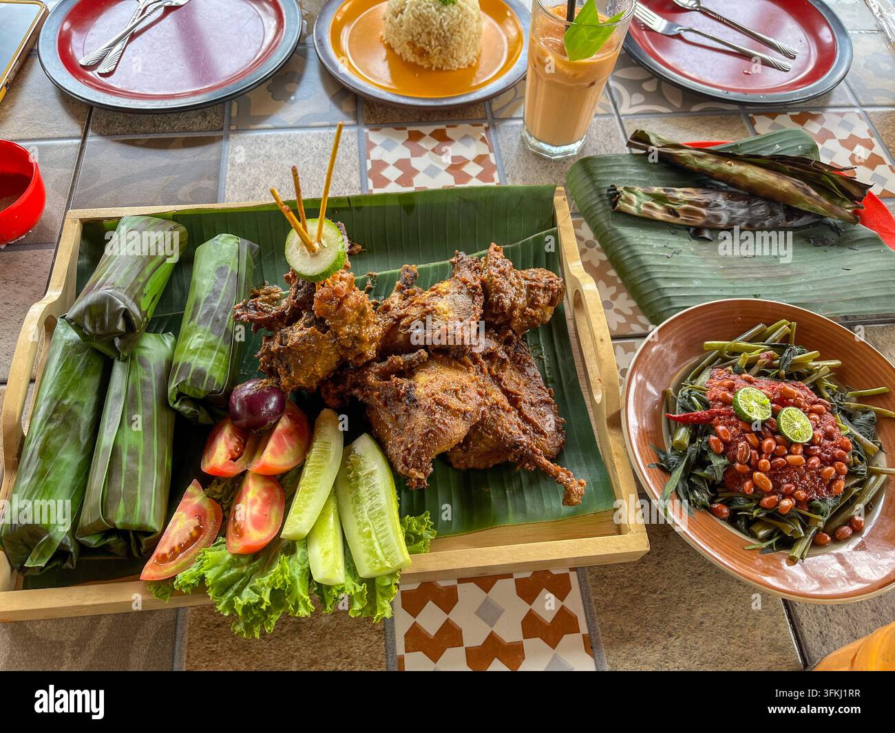 Nasi timbel indonesiano tradizionale con riso avvolto in foglie di banano, pollo fritto, verdure fresche e sambal piccante. Foto Stock