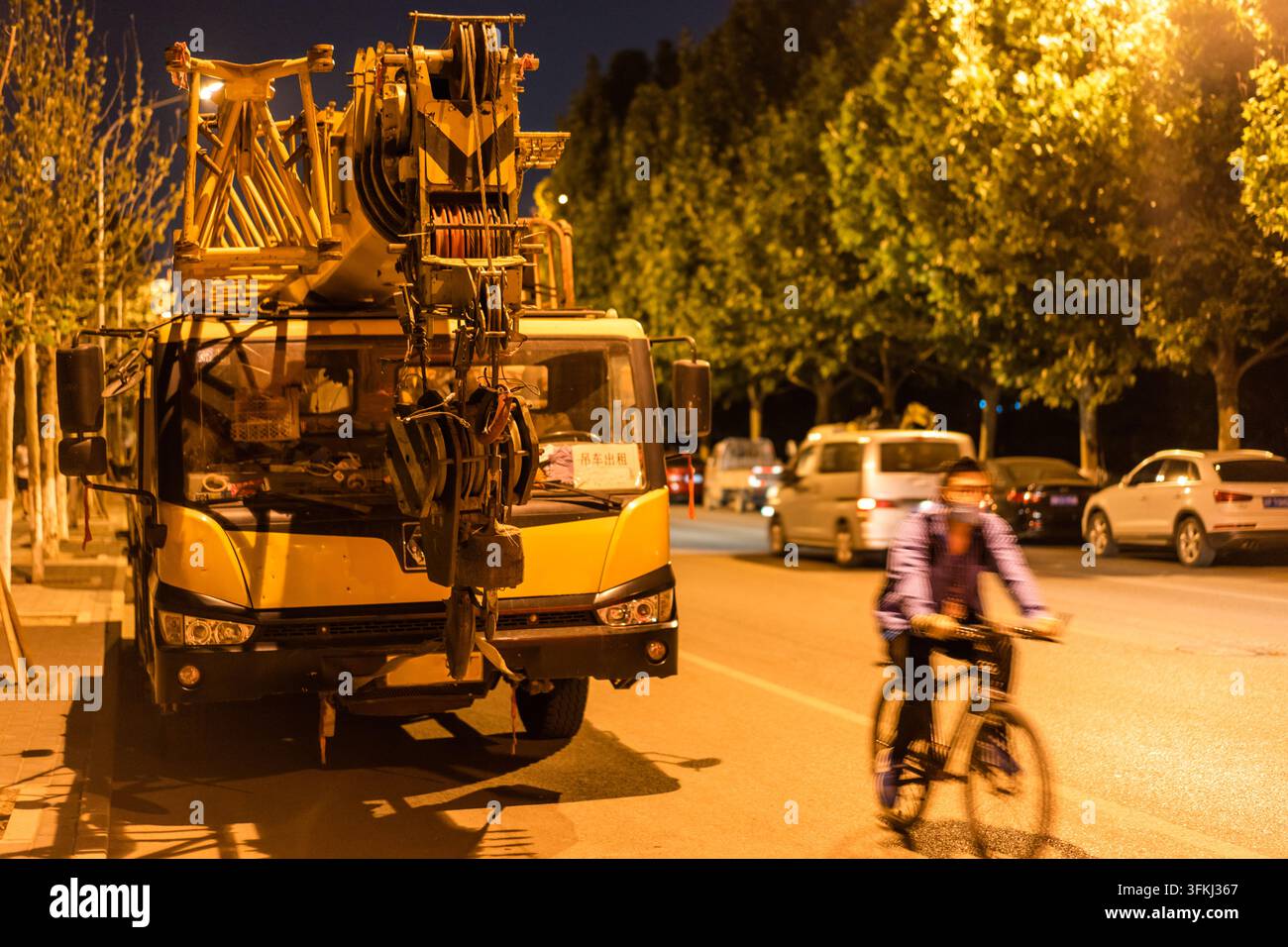 Scena notturna di strada con gru e ciclista che passano Foto Stock