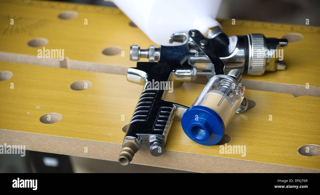 Una pistola a spruzzo di alta qualità e un separatore d'acqua in linea sono posizionati su un banco da lavoro, pronti per l'uso in applicazioni automotive o artistiche Foto Stock