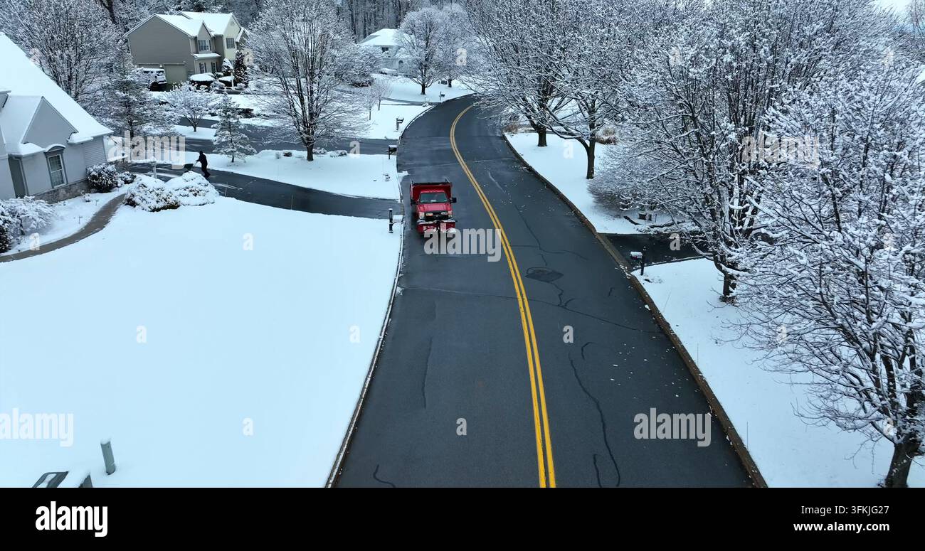 Case di periferia negli USA nella neve invernale. Camion spazzaneve con uomo che sparge sale sul ghiaccio e sui vialetti ghiacciati. Alberi coperti di neve molto belli. Vista aerea, Rohrerstown, Pennsylvania. Foto Stock